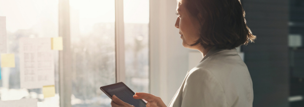 Woman holding a tablet looking out a window.
