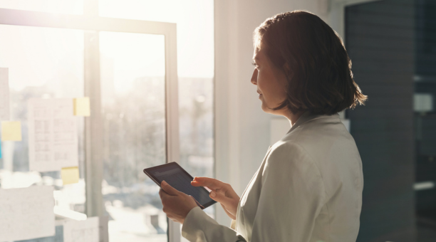 Woman holding a tablet looking out a window.