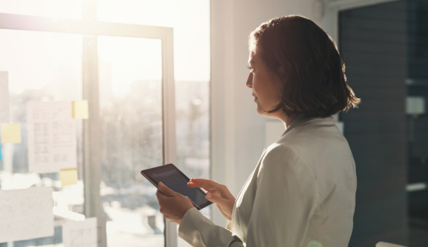 Woman holding a tablet looking out a window.