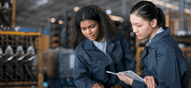 Two women wearing navy jackets looking down at a machine.