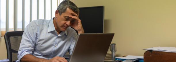 Minority man at work looking depressed while sitting at his desk on a laptop.