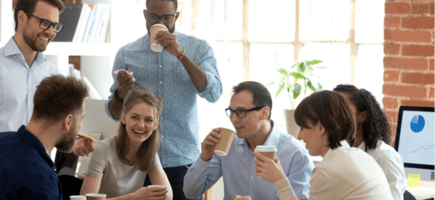 Diverse group of coworkers drinking coffee and laughing while working at a conference table. 