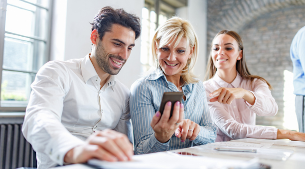 three employees looking at smartphone and smiling