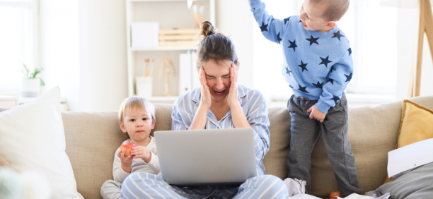Stressed mom sitting on couch with two kids and an open laptop.