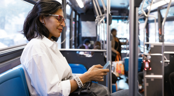 Middle aged woman commuting on a bus while looking down at her phone.